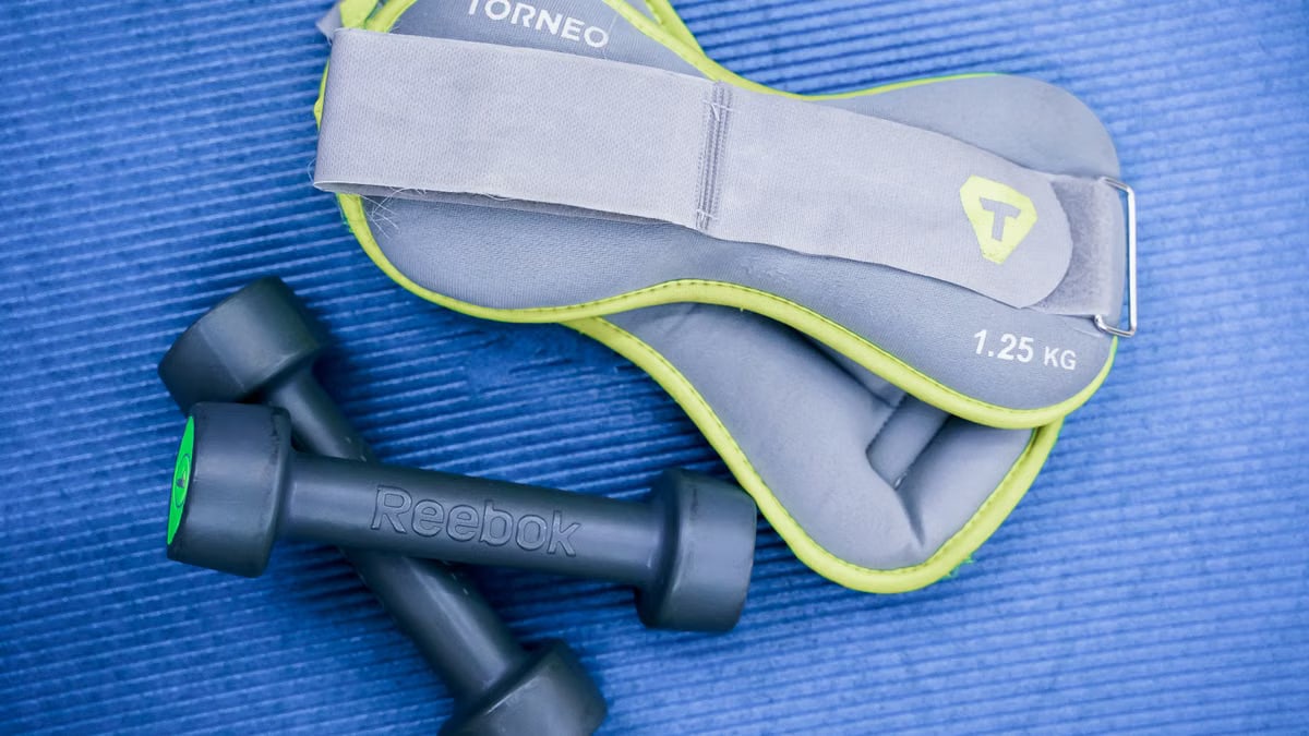 From above of modern dumbbells and leg weight belts placed on blue fitness mat in studio